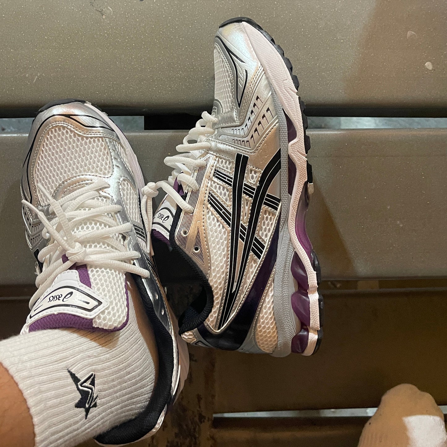 Pair of white running shoes with black and purple accents on a metallic surface.