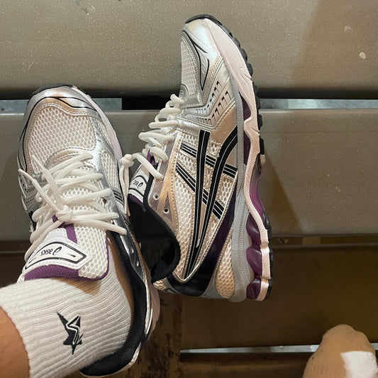 Pair of white running shoes with black and purple accents on a metallic surface.